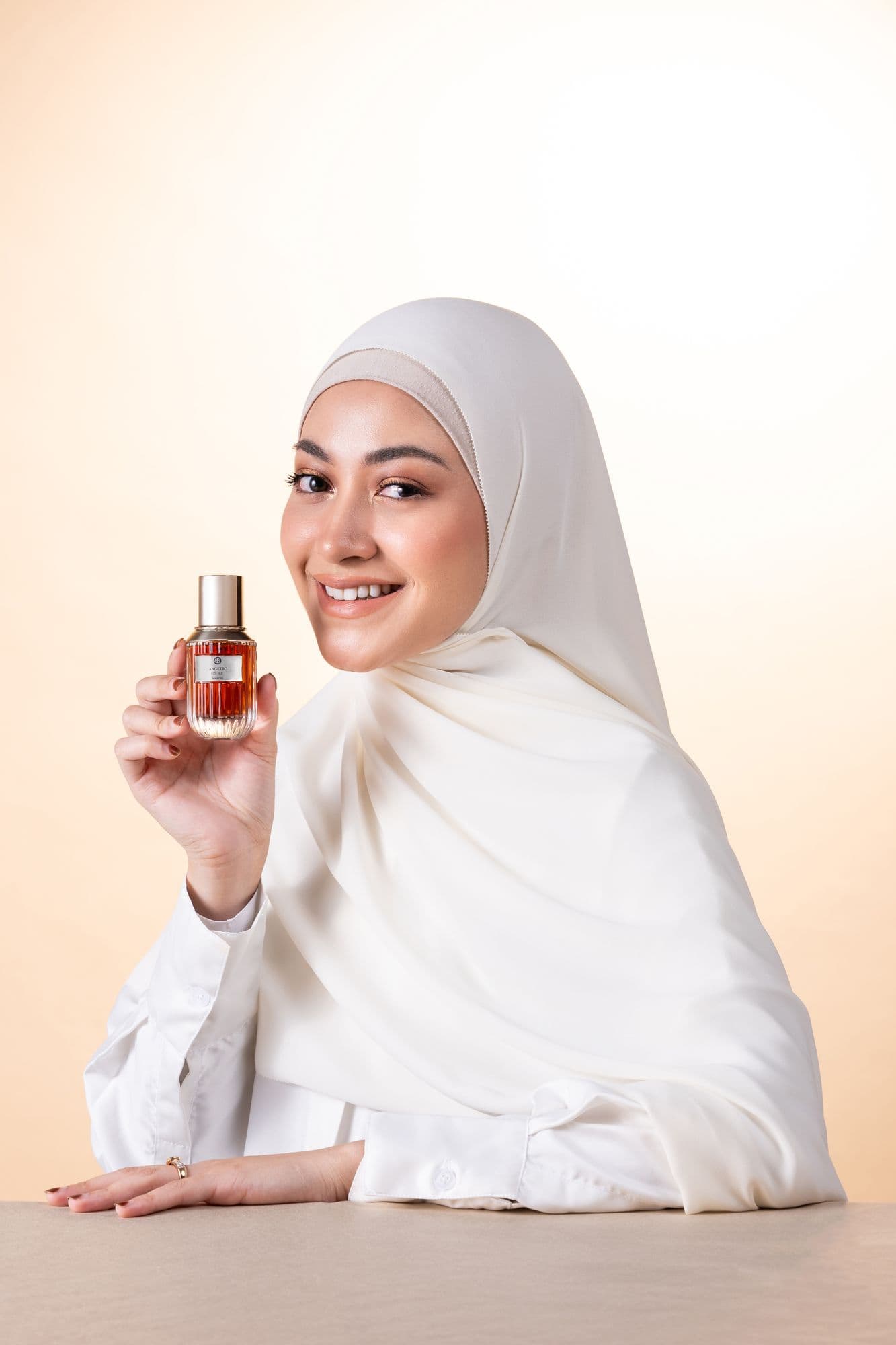 Model in a white hijab holding a Beauboss perfume bottle